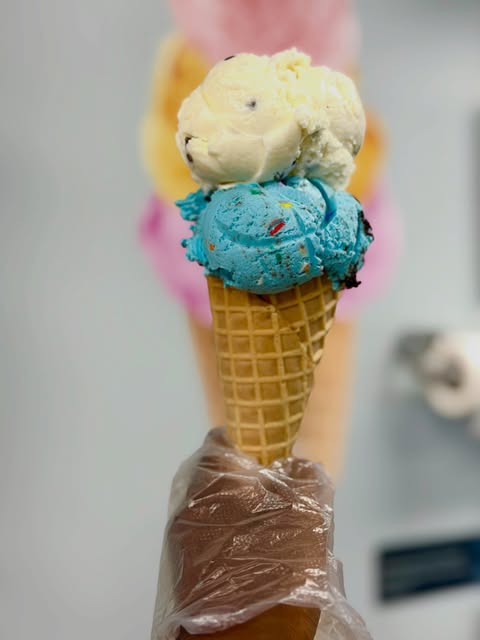 A waffle cone from Taylor's holding a scoop of blue sprinkle ice cream under a scoop of vanilla with chocolate chips