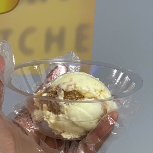 A cup of ice cream held up in front of the yellow Taylor's Cereal Bowl Kitchen sign