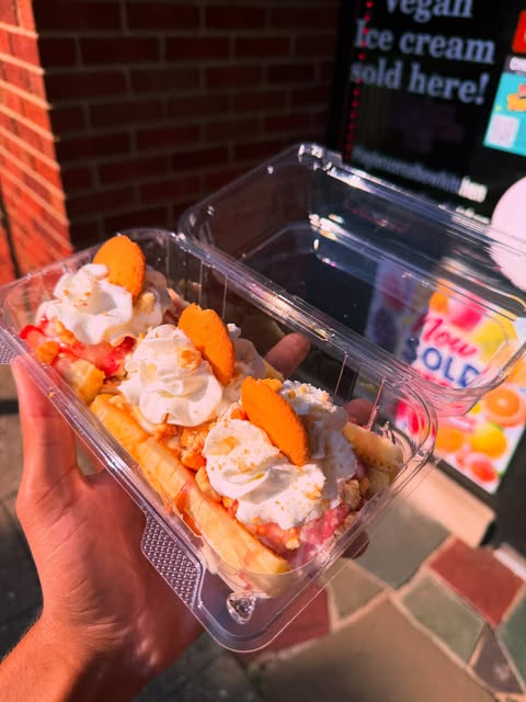 Three banana splits in takeout containers, each topped with whipped cream and a wafer cookie